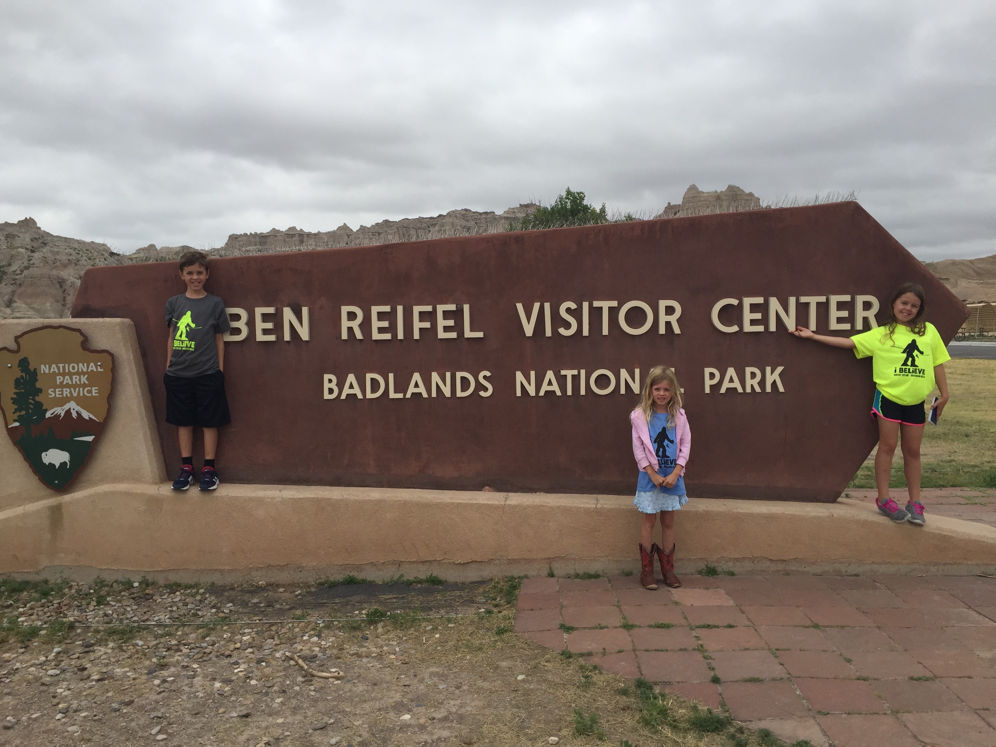 A boy and two girls posing in front of a sign for Ben Reifel Visitor Center