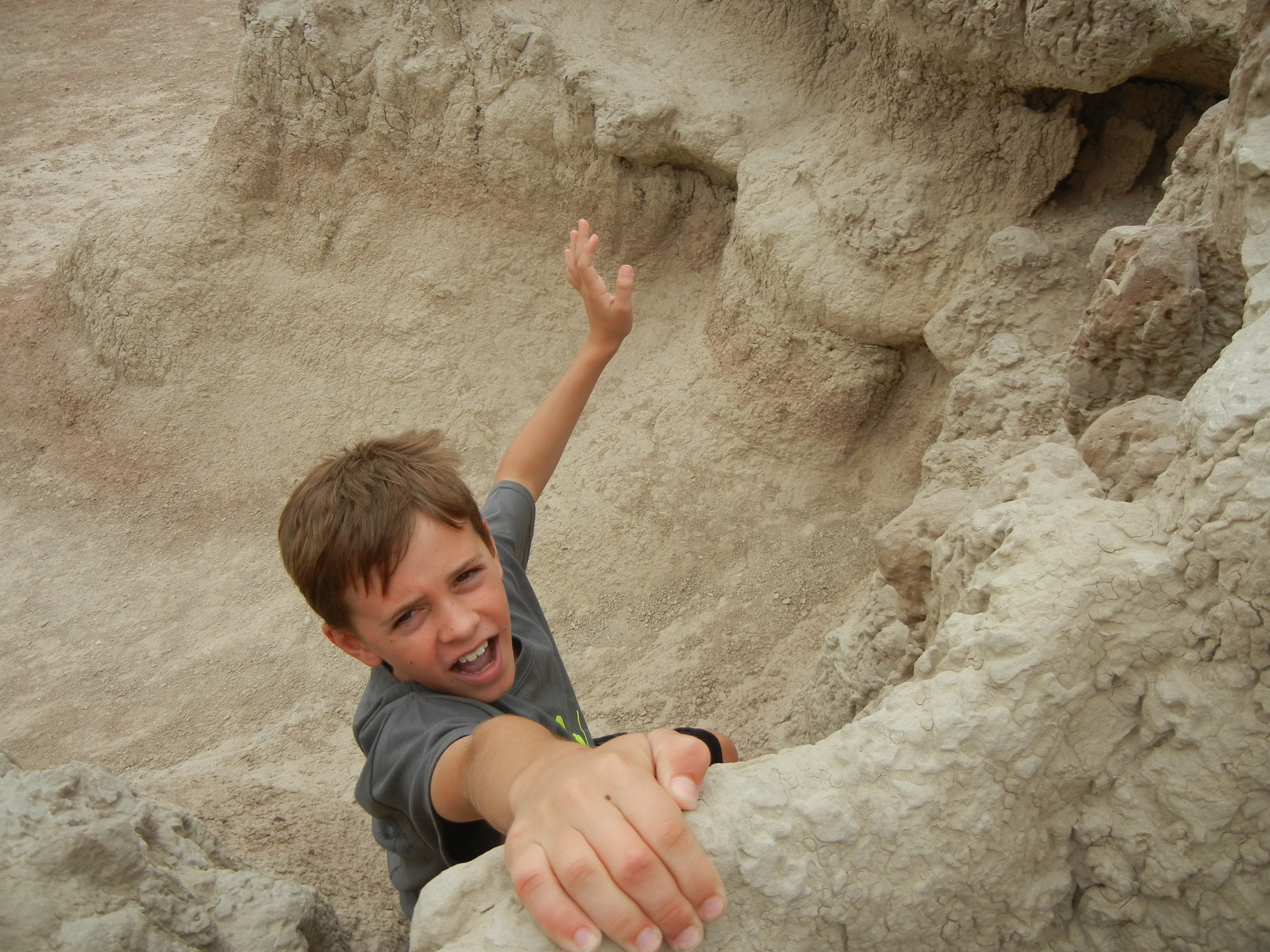 A boy pretending to look alarmed as he hangs from a small rocky hillock