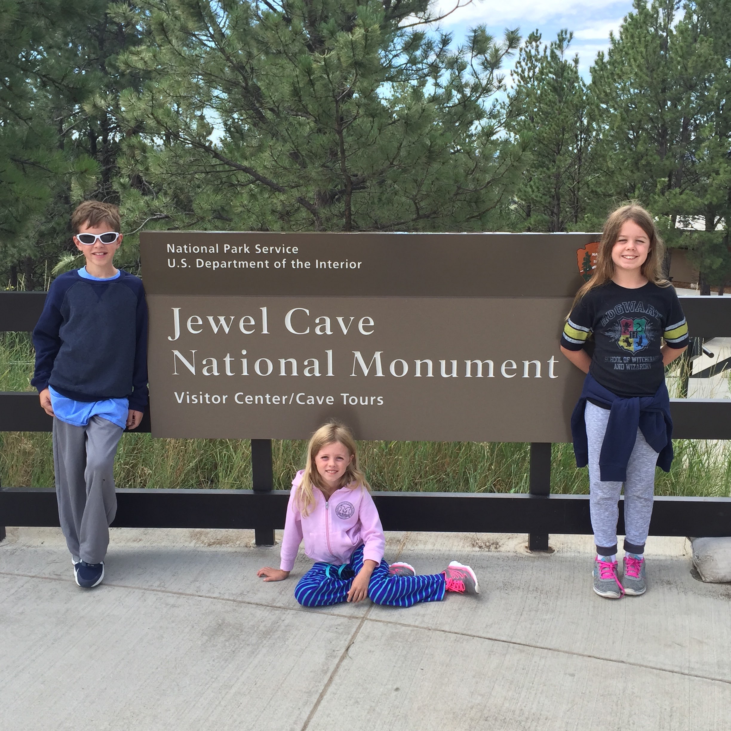 A boy and two girls posing in front of a sign for Jewel Cave National Monument